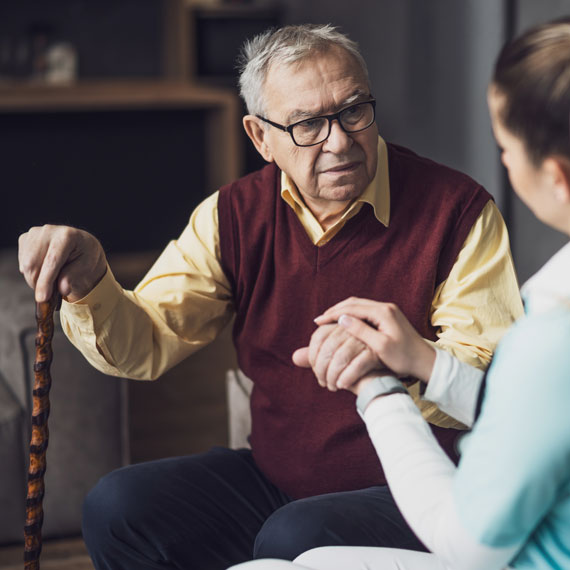 An elderly man and young woman sit together, holding hands showing a moment of connection.