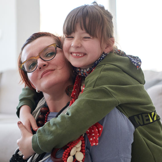 Child affectionately hugs woman whilst sitting together in a warm and inviting space.