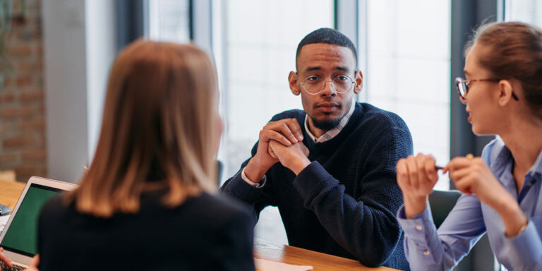 Three people seated at a table discussing and exchanging thoughts.